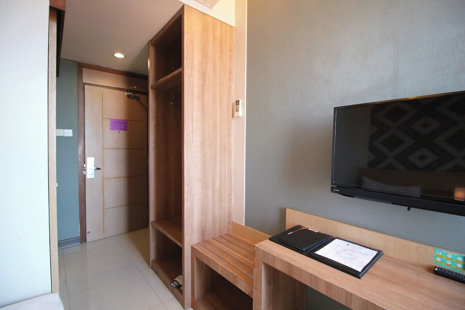 Een hotelkamer met een houten bureau, een flatscreen televisie en een garderobe.