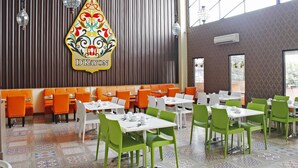 Un ristorante con sedute arancioni, sedie verdi, tavoli bianchi e un cartello decorativo.