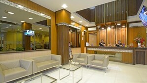 Una hall moderna di un hotel con una reception, una zona salotto e un grande specchio che riflette l'interno.