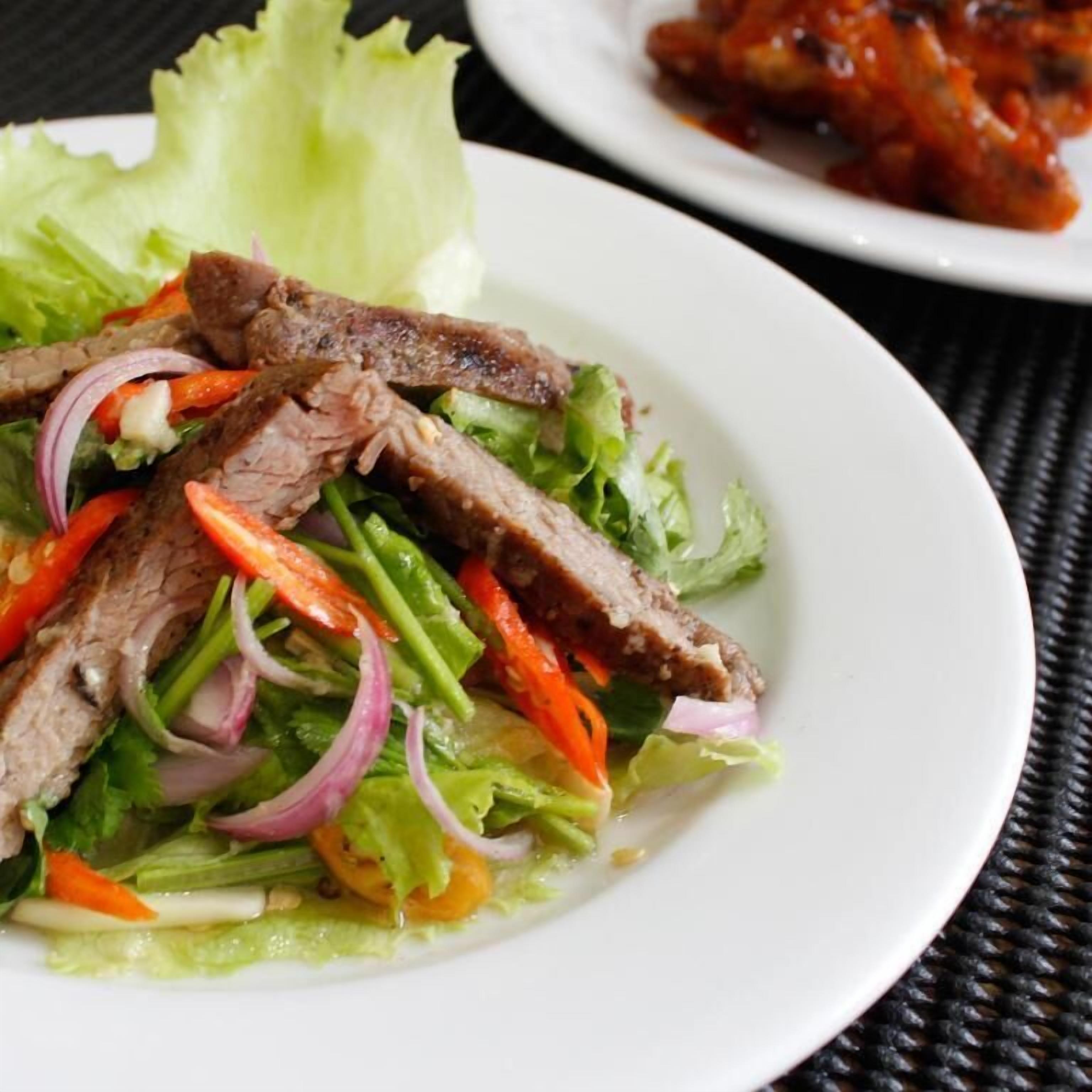 A plate of sliced beef with vegetables on a white plate.