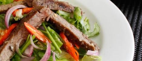 A plate of sliced beef with vegetables on a white plate.