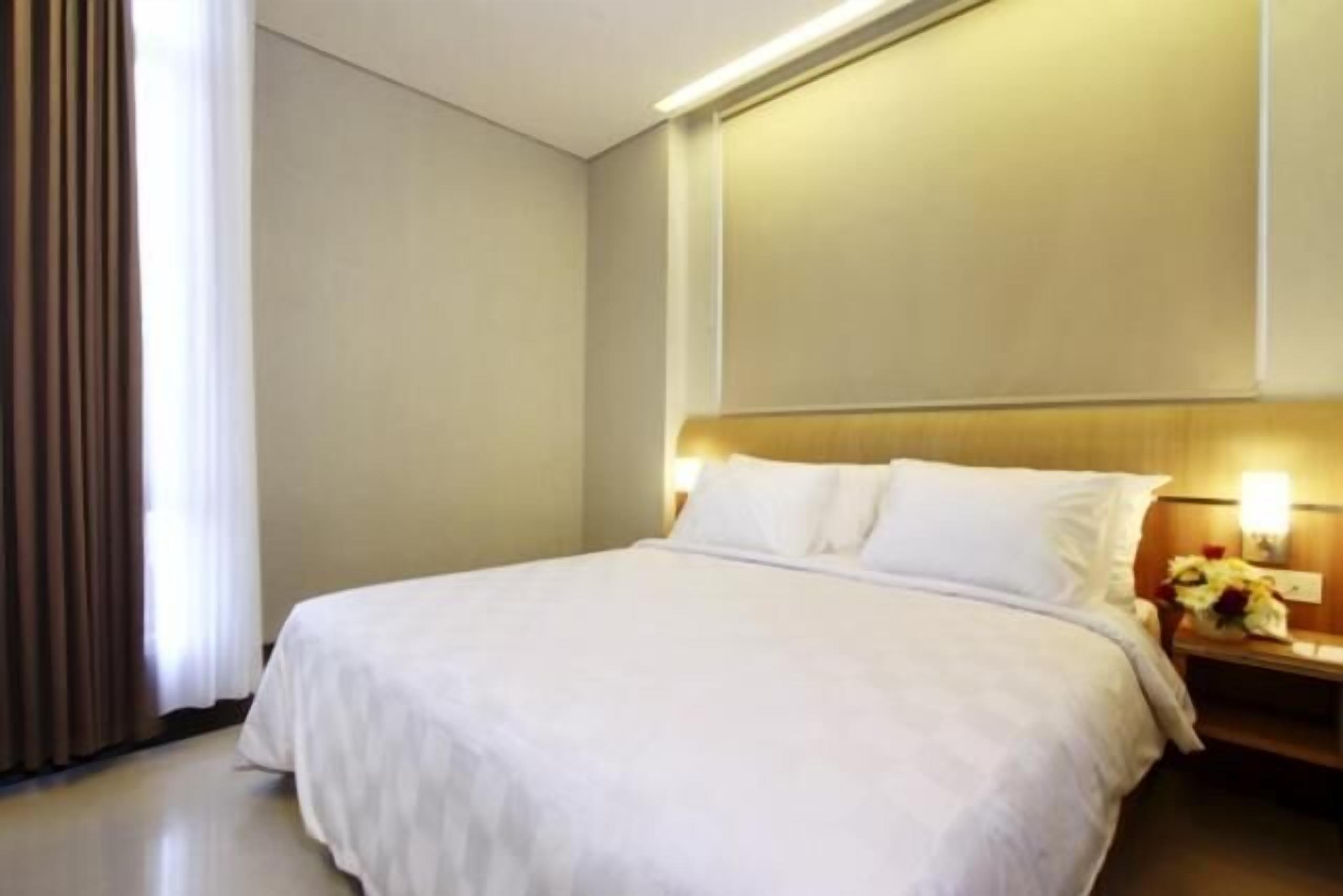 A hotel room with a large bed, a nightstand with a lamp, and a window with curtains.