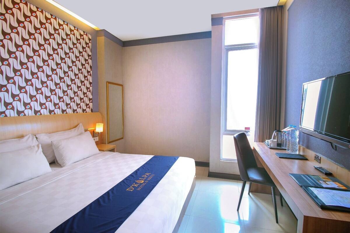 A hotel room with a bed, a desk, a TV, a chair, and a window.