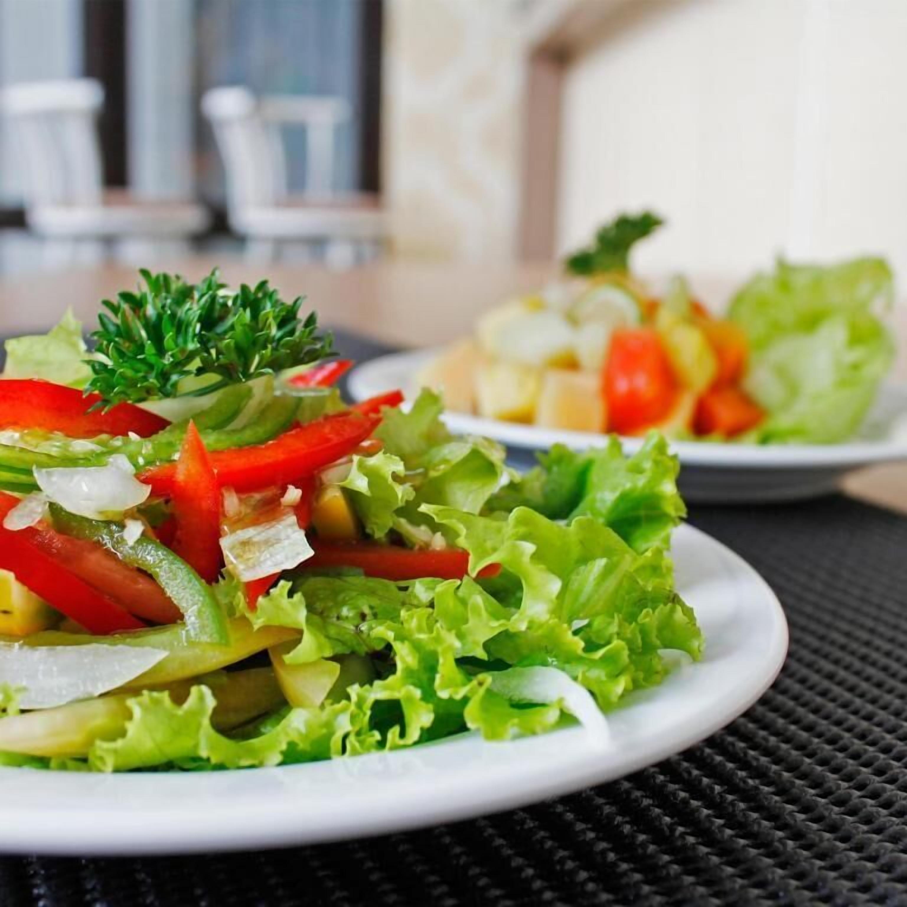 A plate of mixed greens salad with red bell peppers and onions.