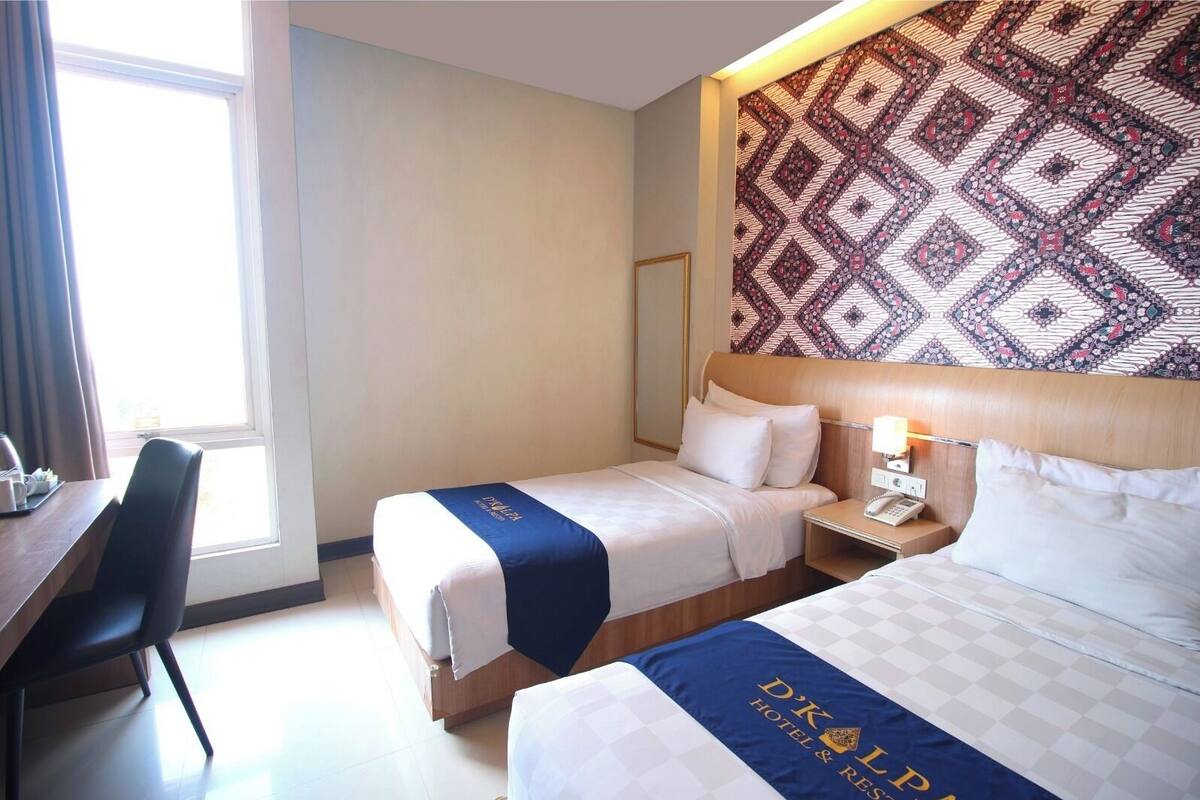 A hotel room with two beds, a desk, a chair, a patterned wall, and a window.