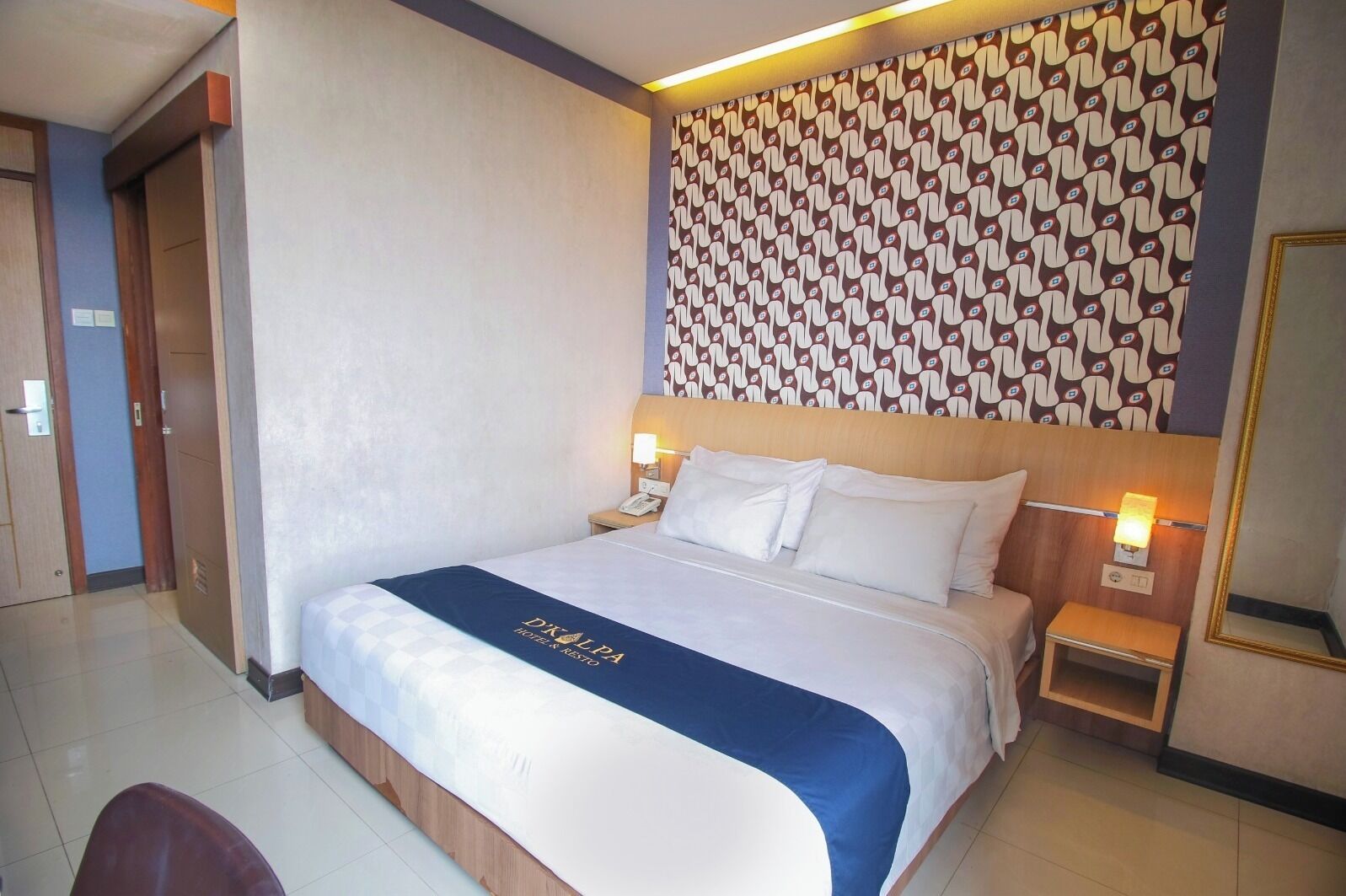 A hotel room with a bed, bedside tables, a patterned wall, and a sign on the bed.