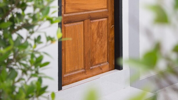 A wooden door with a black frame, set in a white wall, with a wall-mounted light fixture to the right. - Triple Tree Resort (Lam Luk Ka)
