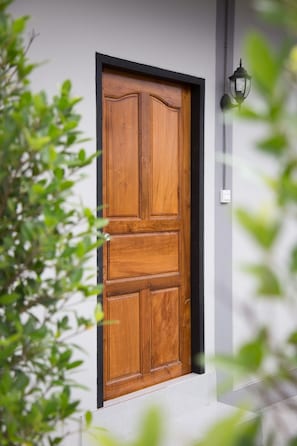 A wooden door with a black frame, set in a white wall, with a wall-mounted light fixture to the right. - Triple Tree Resort (Lam Luk Ka)