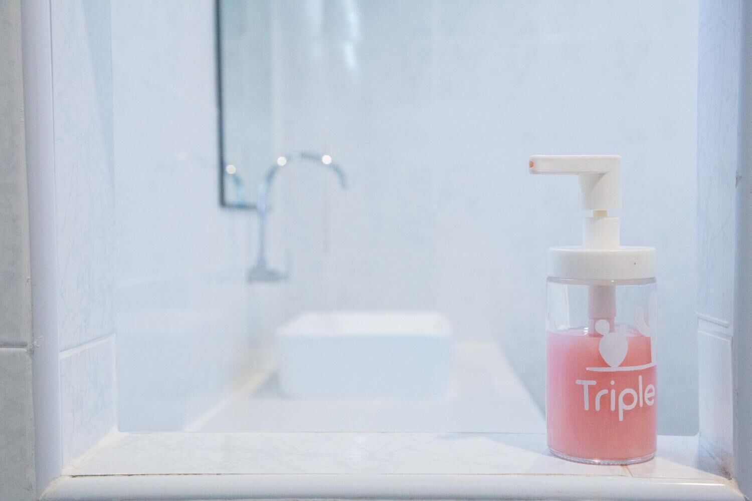 Un baño con un lavabo blanco, una botella de vidrio de Triple desinfectante de manos y un espejo sobre el lavabo.
