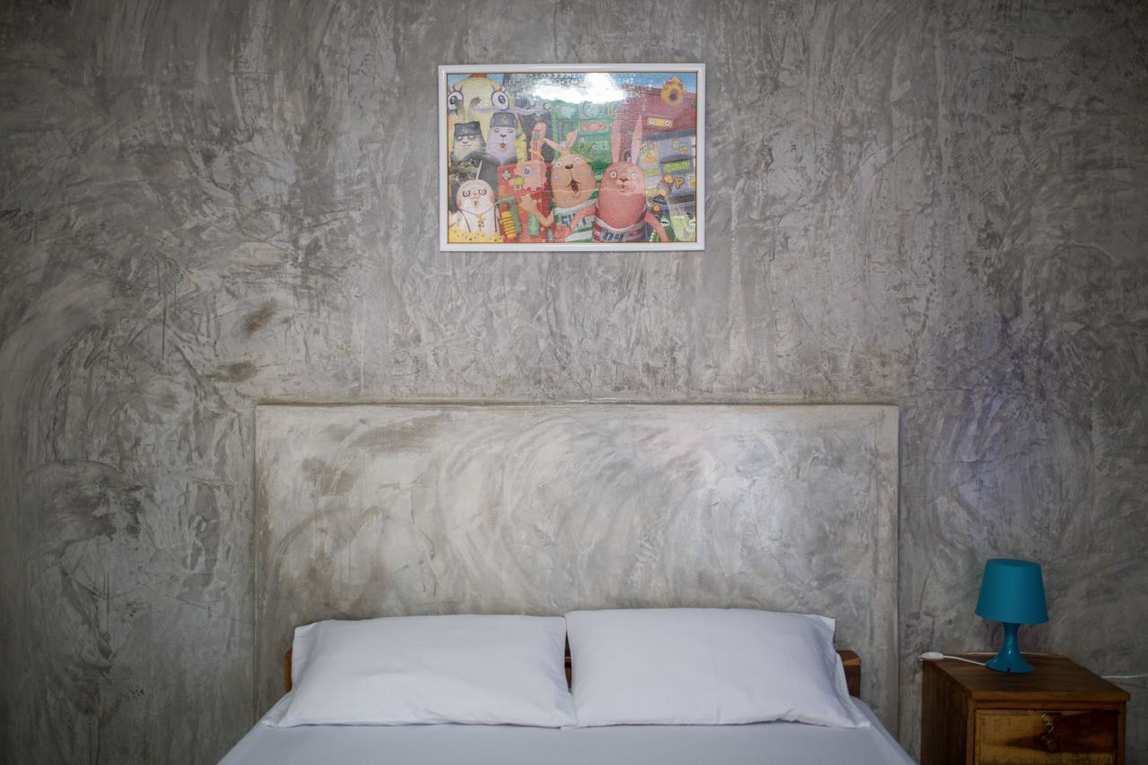 A bedroom with a bed, a nightstand with a lamp, and a wall with a framed picture.