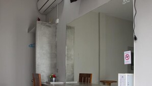 A room with a long, narrow desk, a chair, a large mirror, an air conditioning unit, and a television mounted on the wall. - Triple Tree Resort (Lam Luk Ka)