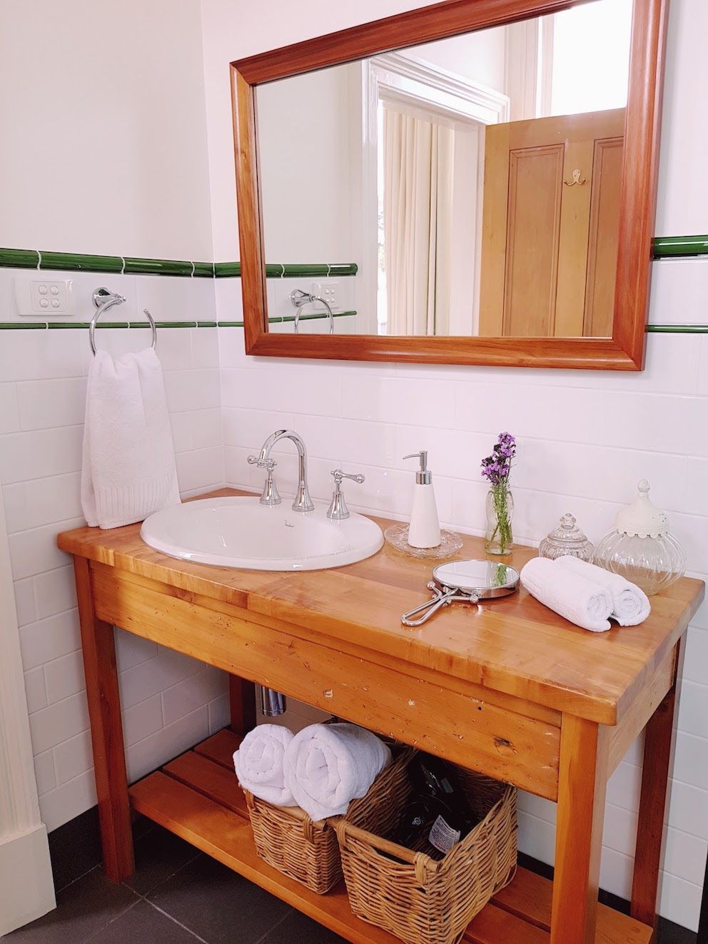 Un baño con tocador de madera, dos lavamanos, un espejo y una cesta de toallas.