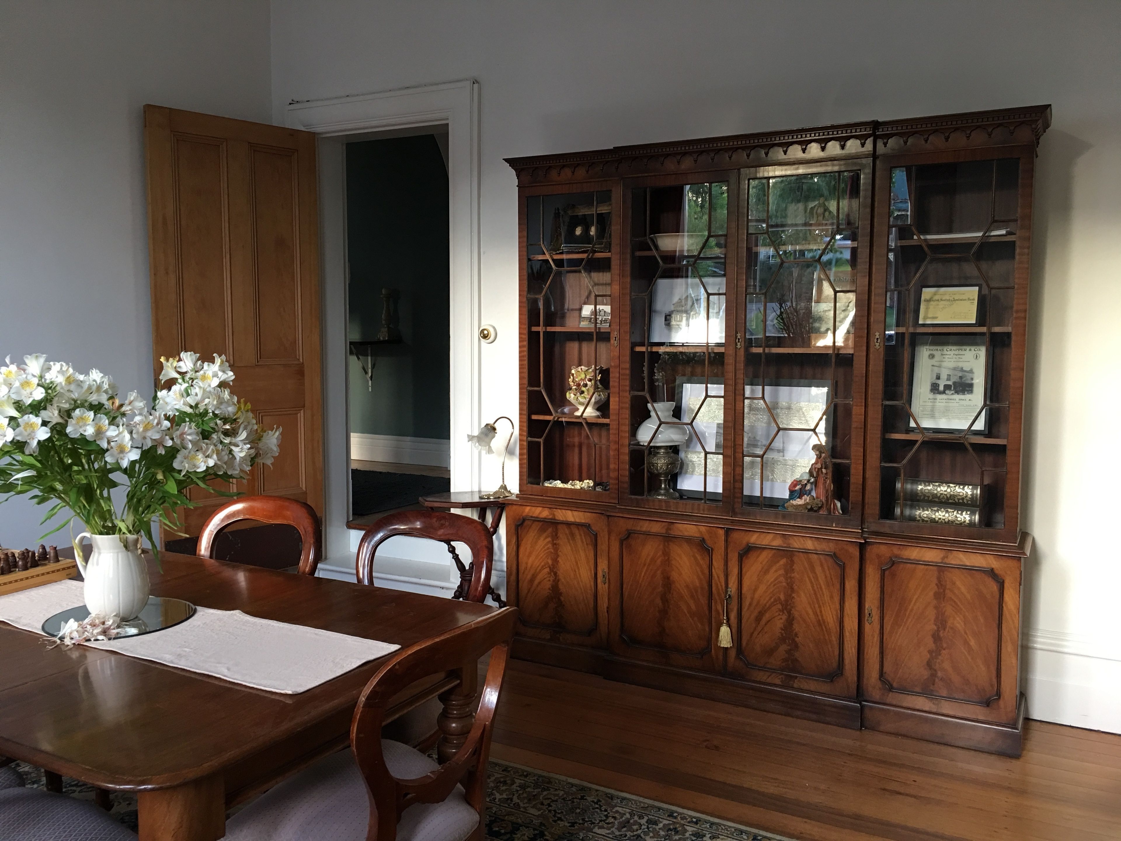 Un comedor con una mesa de madera, sillas, un jarrón de flores y un aparador con puertas de cristal.