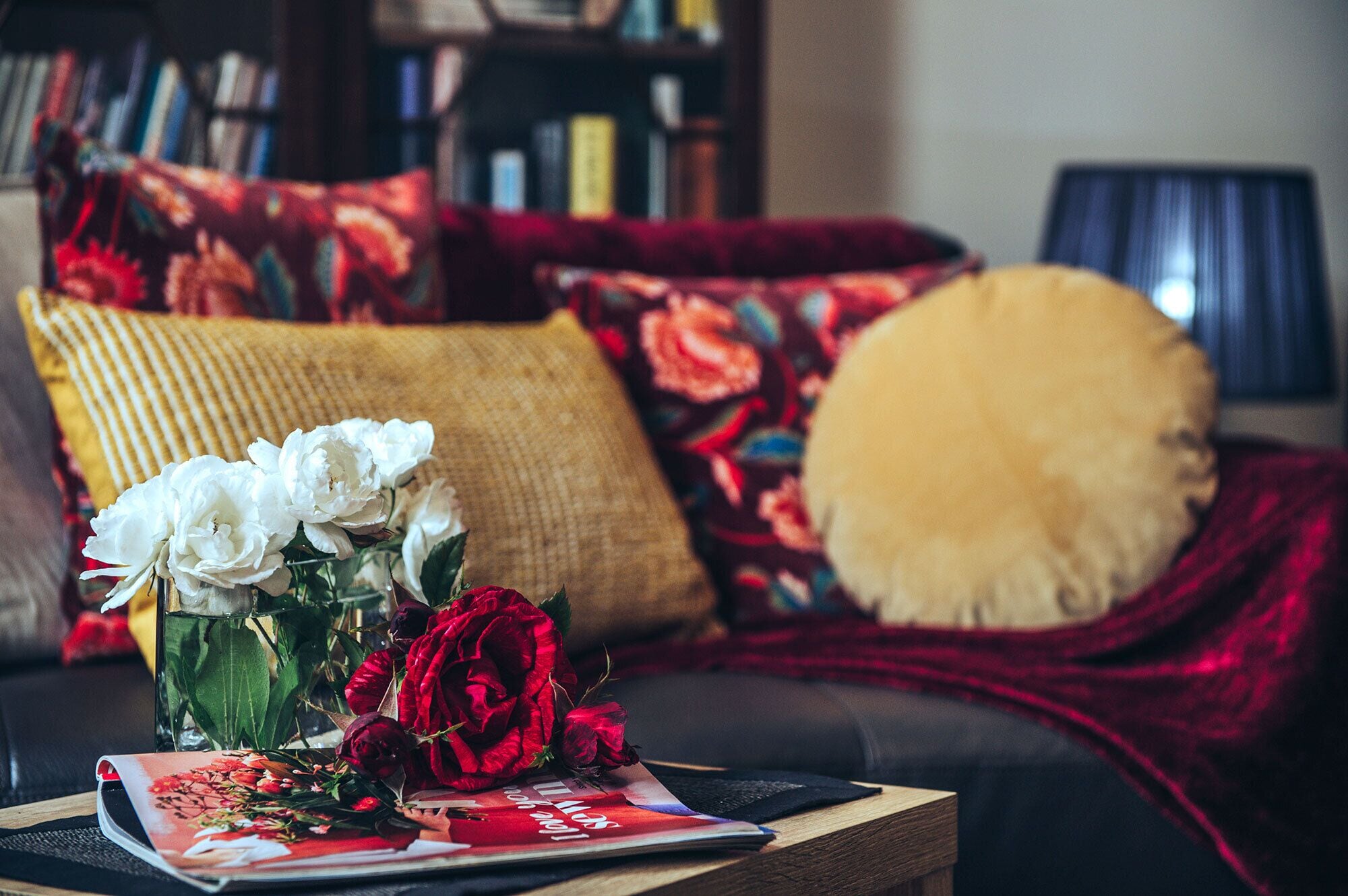 A living room with a sofa, a coffee table with a magazine, and a vase with white and red flowers.