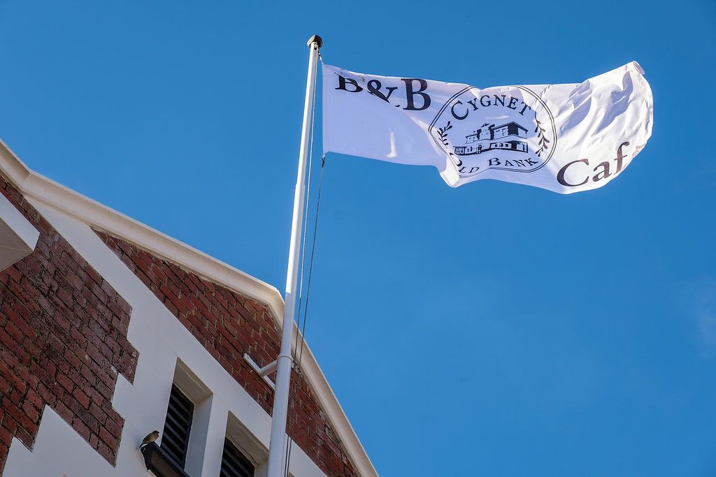 A flag with 'B&B Cygnet Hotel Bank Cafe' text and a building with a brick facade.