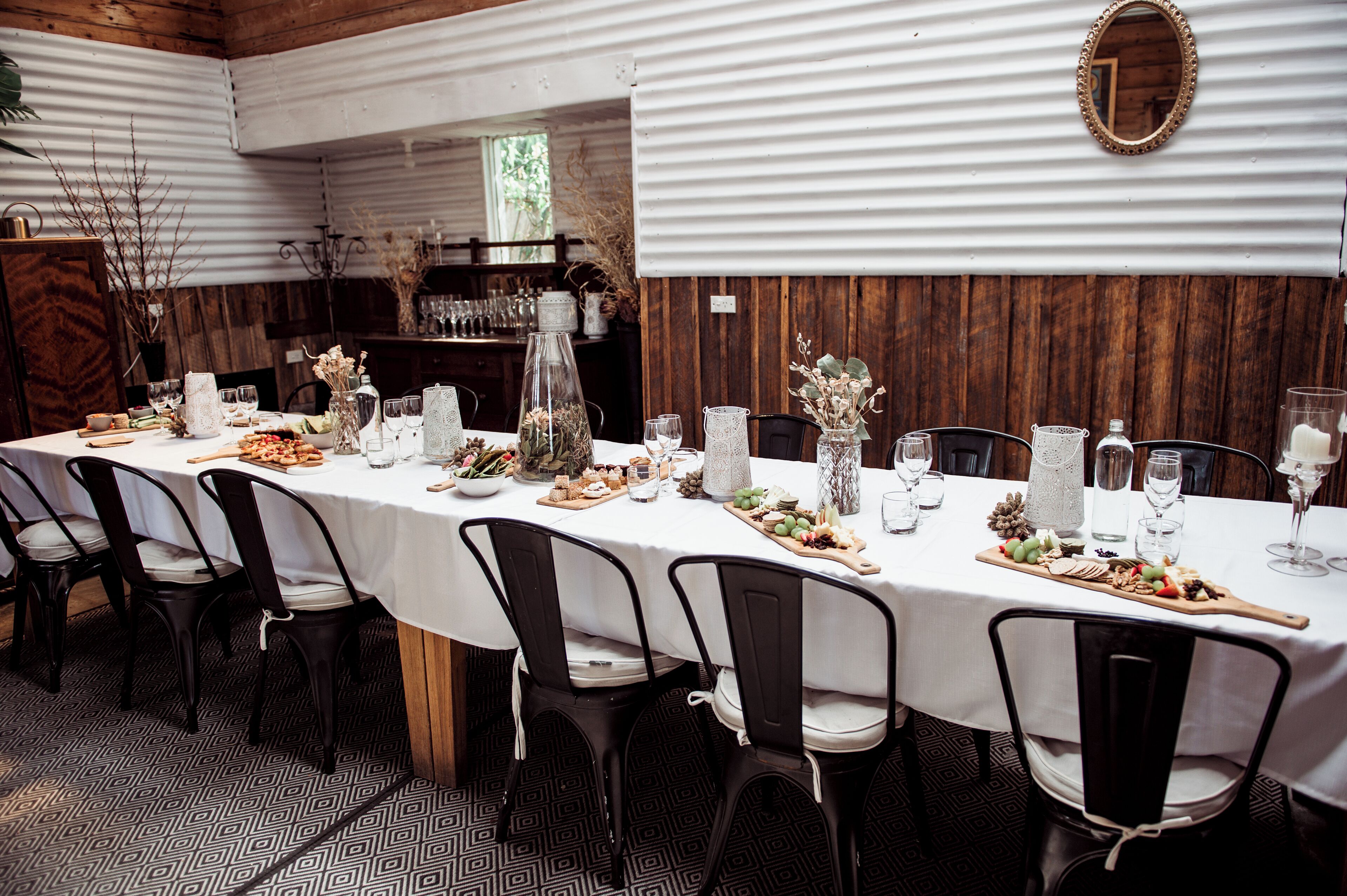 Mesa de jantar comprida com toalha branca, cadeiras pretas e diversos alimentos e bebidas.