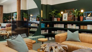 Una biblioteca moderna con sofás de cuero, mesas de centro de madera y estanterías llenas de libros y plantas en macetas.