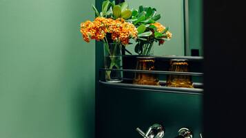 A bathroom with a white sink, a mirror, and a vase with orange flowers. There are three bottles on the sink.