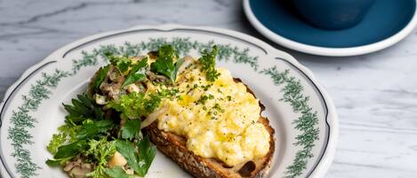 A plate with scrambled eggs and mushrooms on toast, accompanied by a cup of coffee on a saucer.