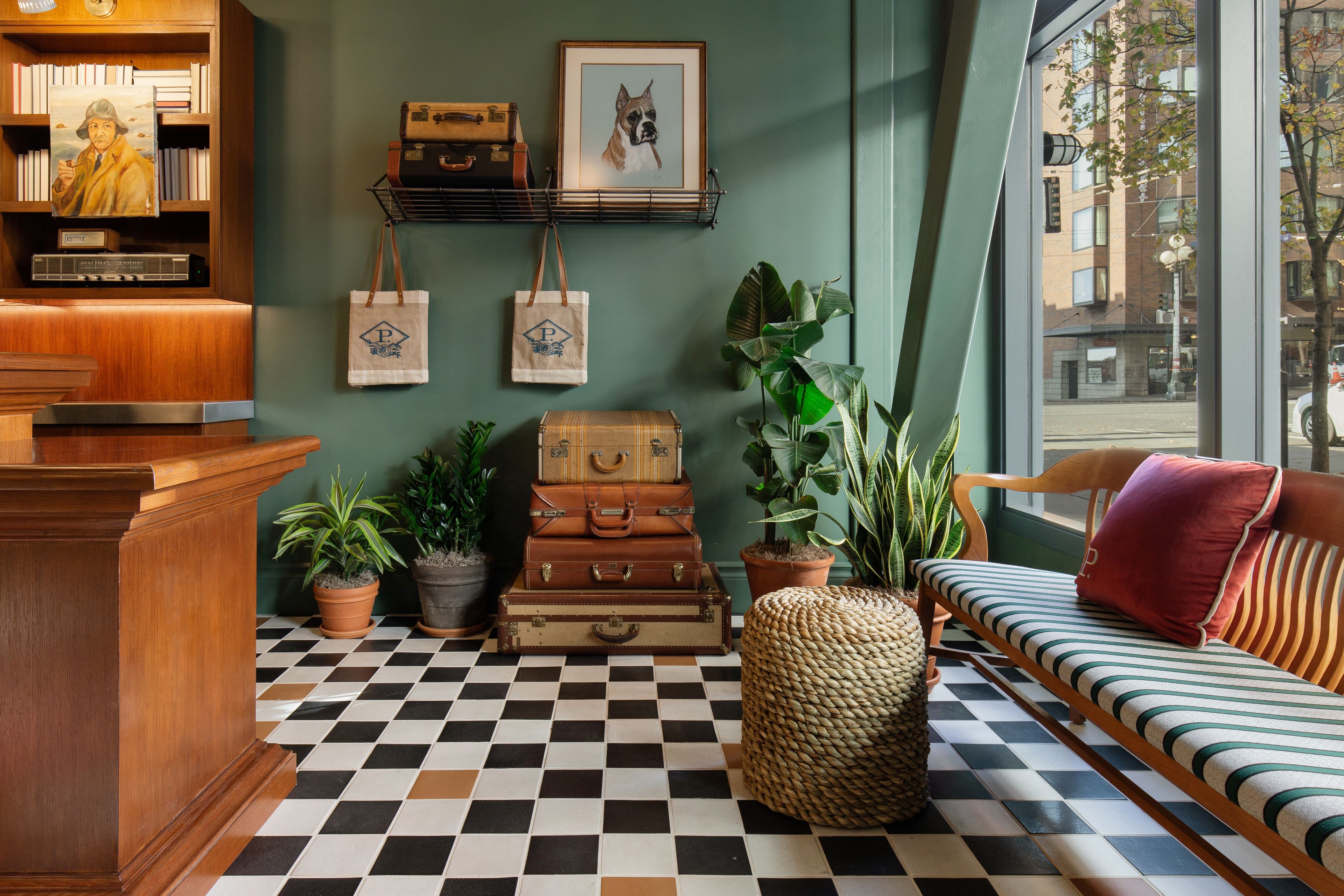 A cozy room with a checkered floor, a wooden desk, a sofa with striped cushions, and a window with a view of buildings.