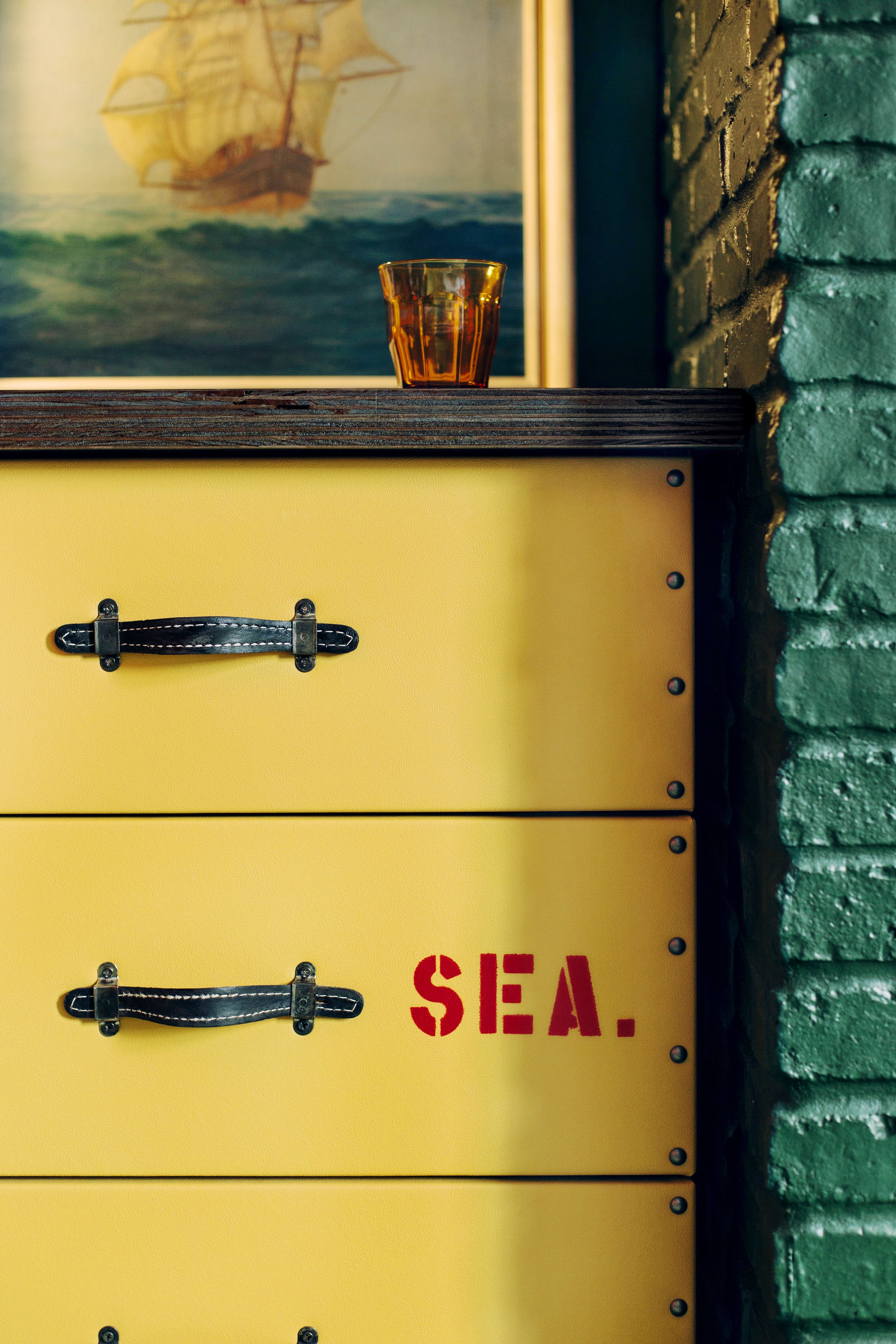 Une commode jaune avec des poignées en cuir noir et le mot « MER » écrit dessus.