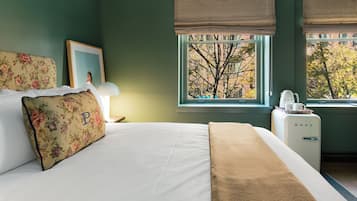 Quarto com cama, mesa de cabeceira, luminária, janela com vista para árvores e um frigorífico de estilo vintage.