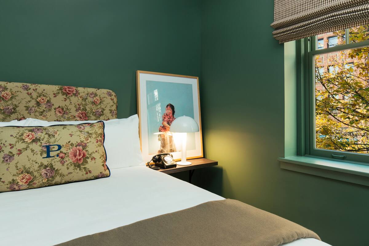 A neatly made bed with floral pillows, a bedside lamp, and a framed picture on a nightstand.