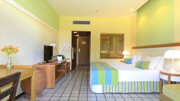 Una habitación de hotel con cama, escritorio, silla, televisión y ventana con persianas.