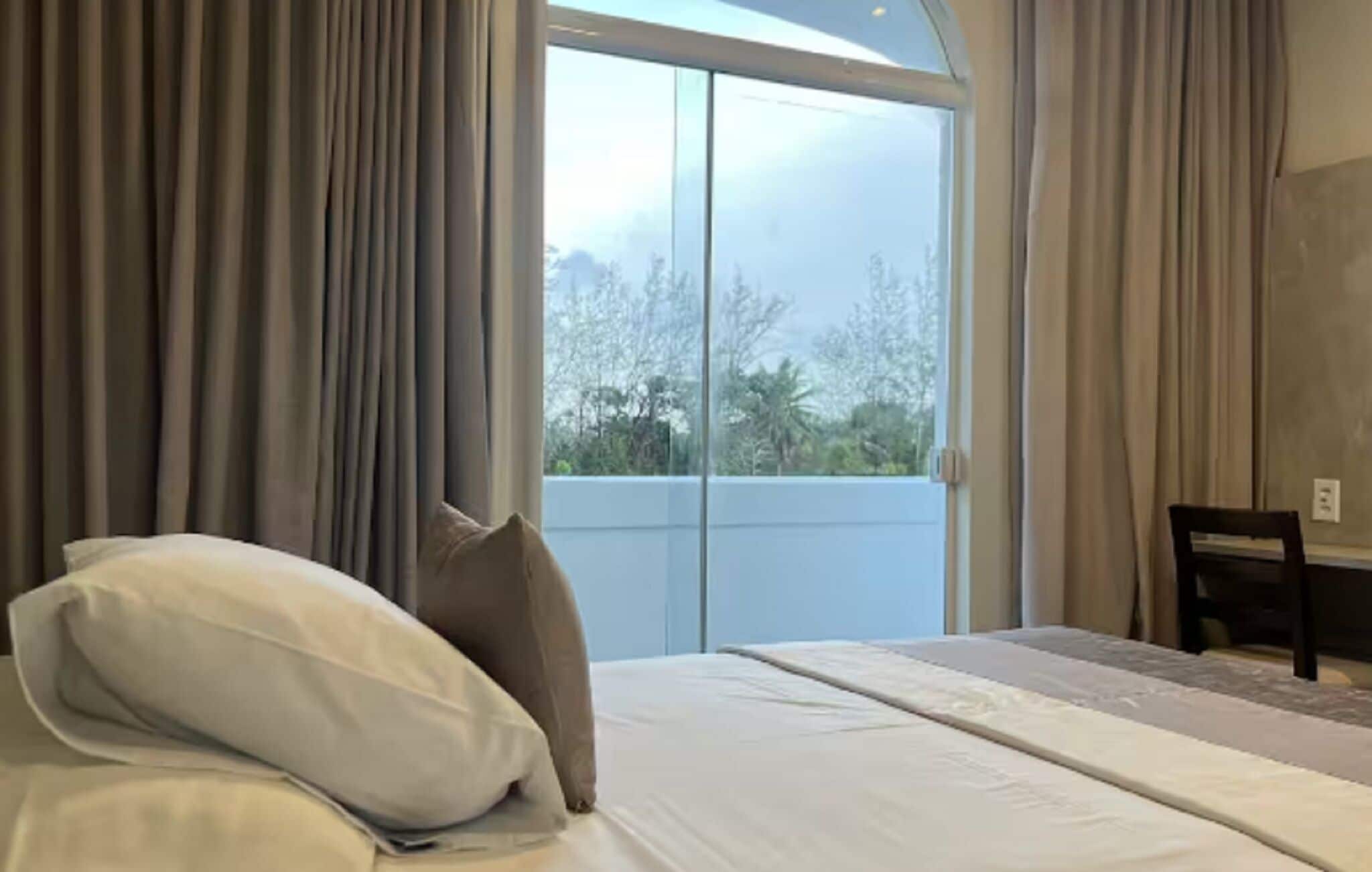 Un dormitorio con una cama grande, una silla y vistas al exterior a través de un ventanal.