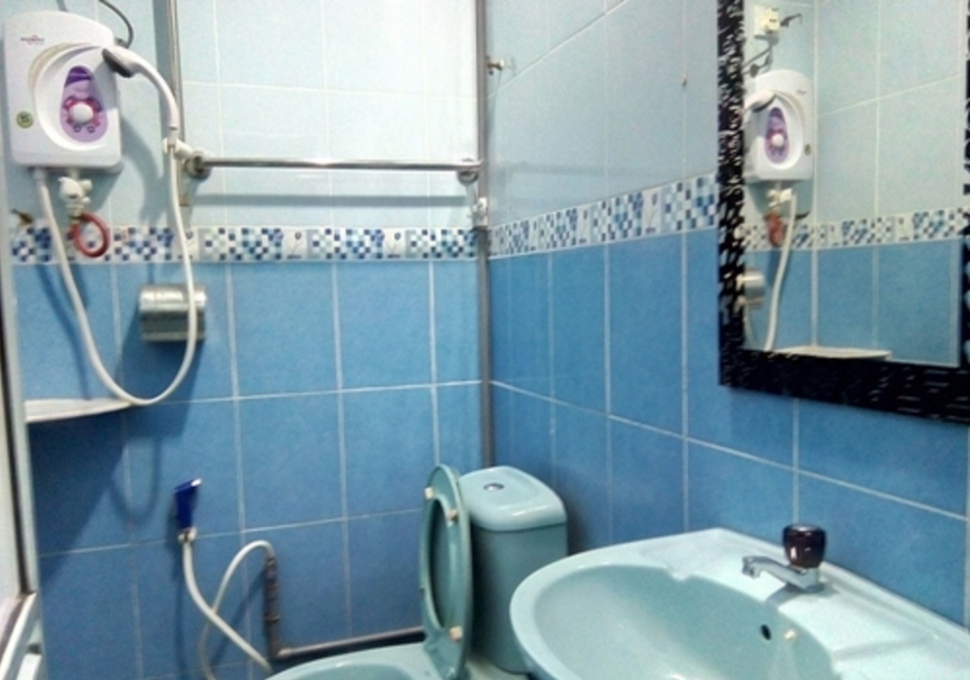 A bathroom with blue tiles, a sink, a mirror, and a toilet.