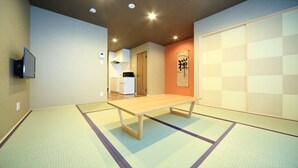 Ein Zimmer mit Tatami-Böden, einem Holztisch, einem Fernseher, einer Küchenzeile und einer Schiebetür.