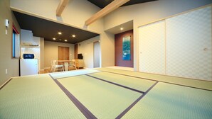 Ein Raum mit Tatami-Matten, einem Holztisch und Stühlen, einem Fernseher und einer Schiebetür.