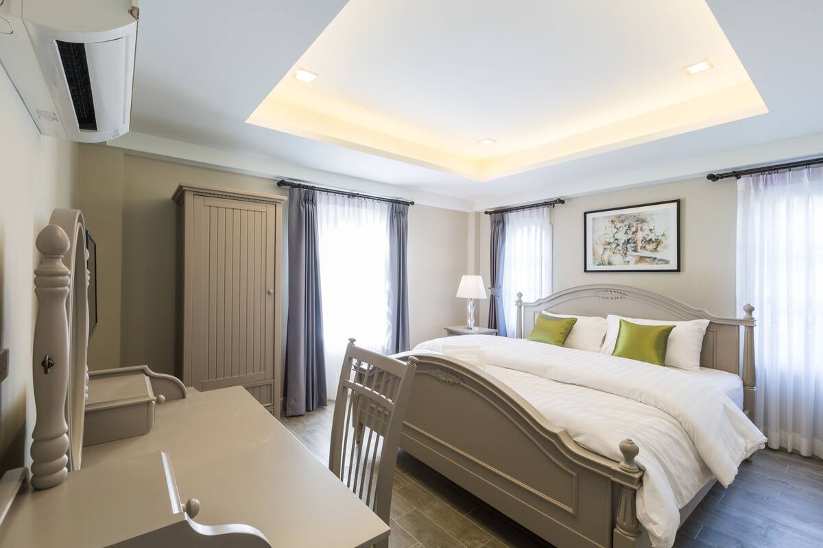 A bedroom with a bed, bedside table, chair, and a ceiling light fixture.