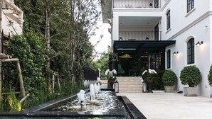 Entrada de hotel com um recurso de água, plantas em vasos e área externa bem cuidada.