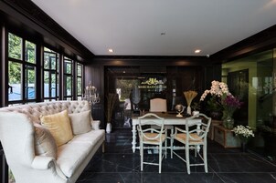 A luxurious room with a large window, a plush sofa, a dining table with chairs, and a view of the outside.