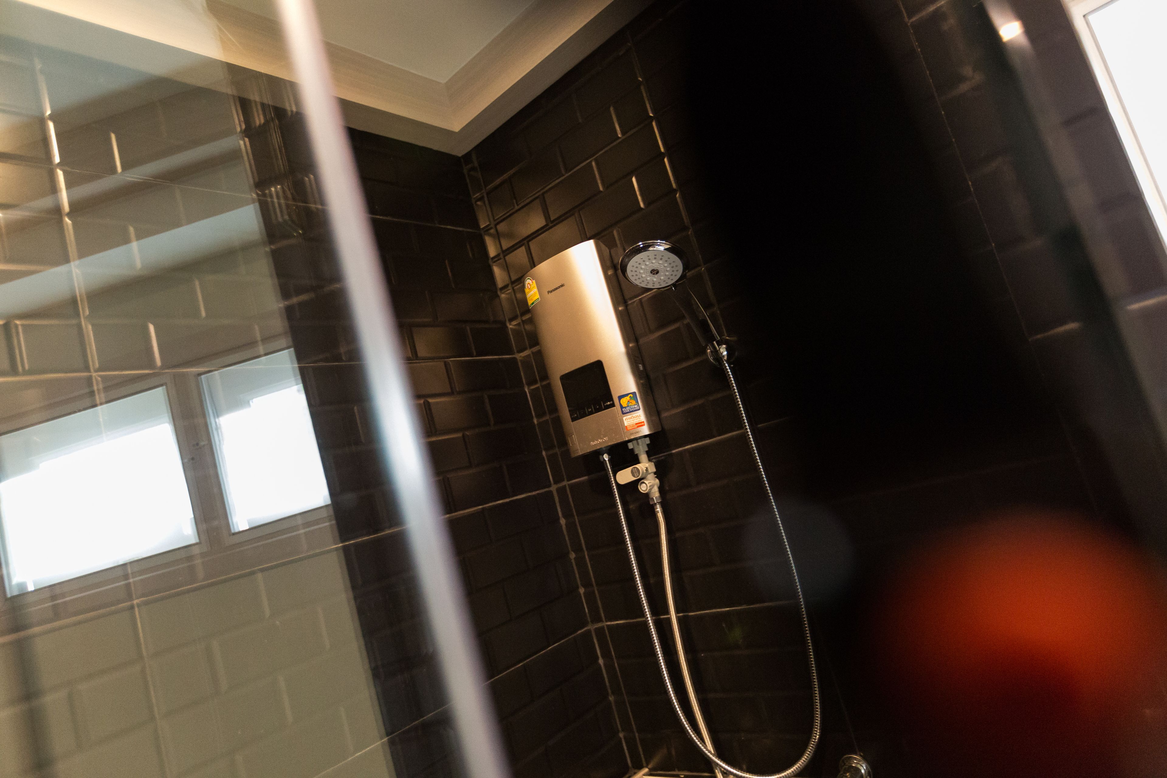 A bathroom with a black tiled wall, a showerhead, and a control panel.