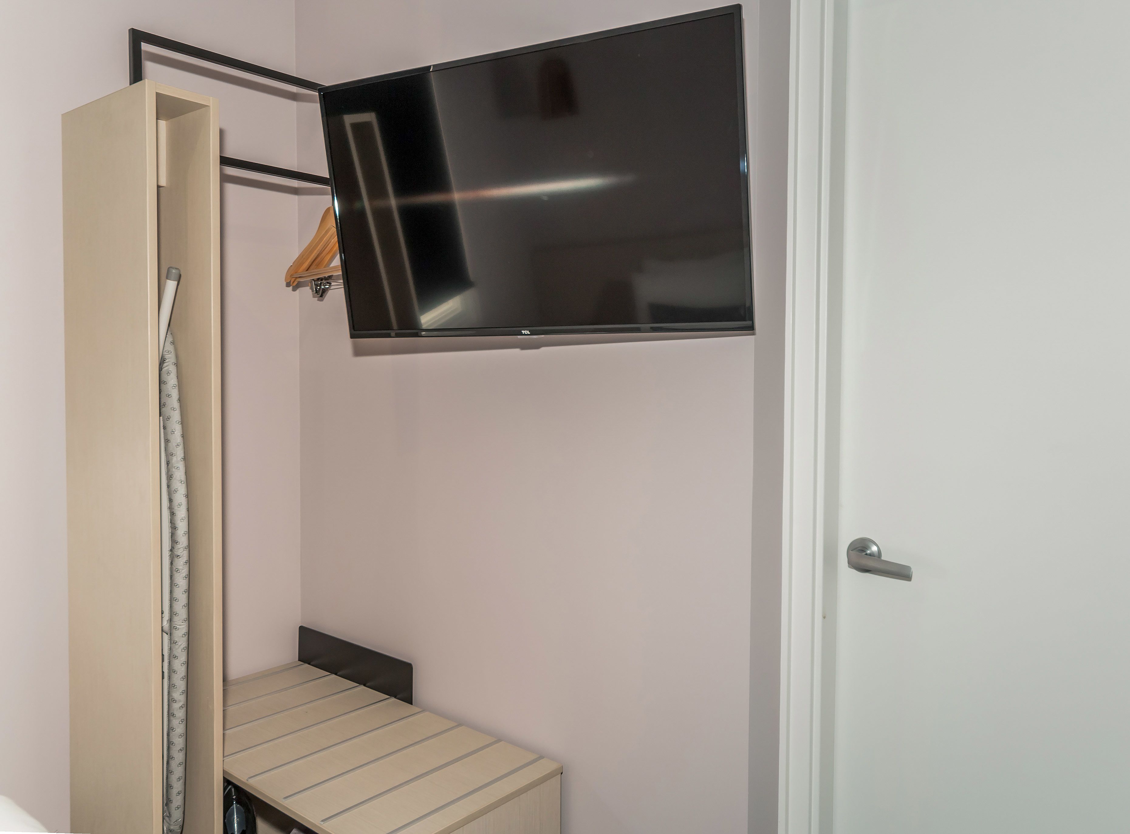 Una habitación con una cama, un televisor montado en la pared y una puerta.