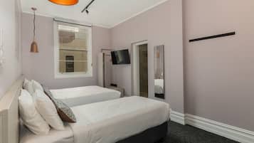 A bedroom with two beds, a TV, a mirror, and a window.