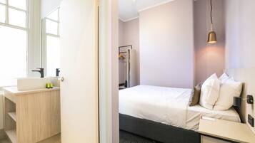 A modern hotel room with a bed, bedside table, and a bathroom with a sink and mirror.
