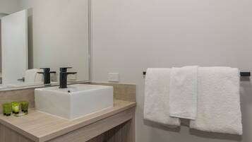 A bathroom with a white sink, black faucet, and a mirror. There are two green bottles on the counter.