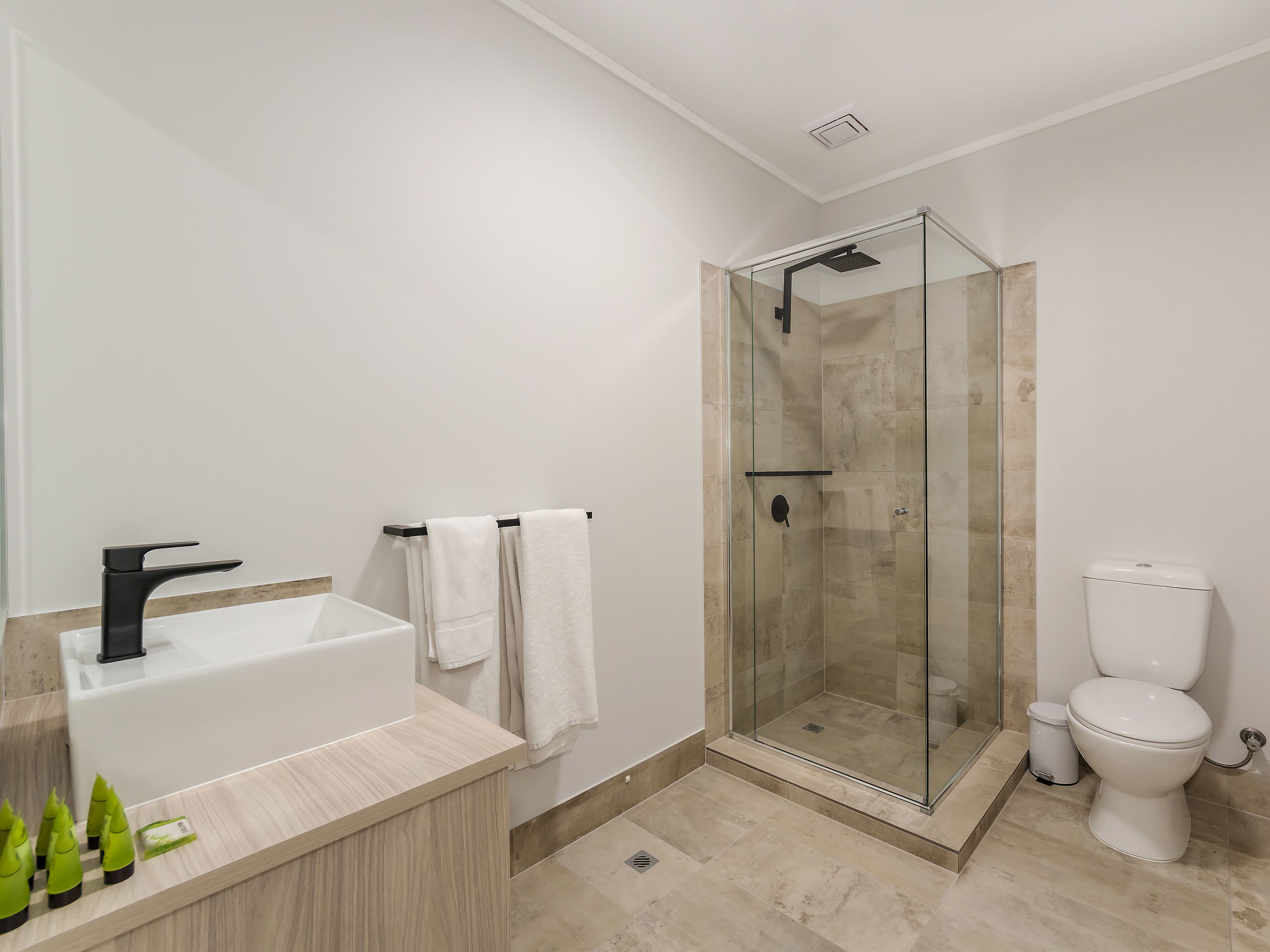 A modern bathroom with a glass-enclosed shower, a white toilet, and a wooden vanity with a black faucet.