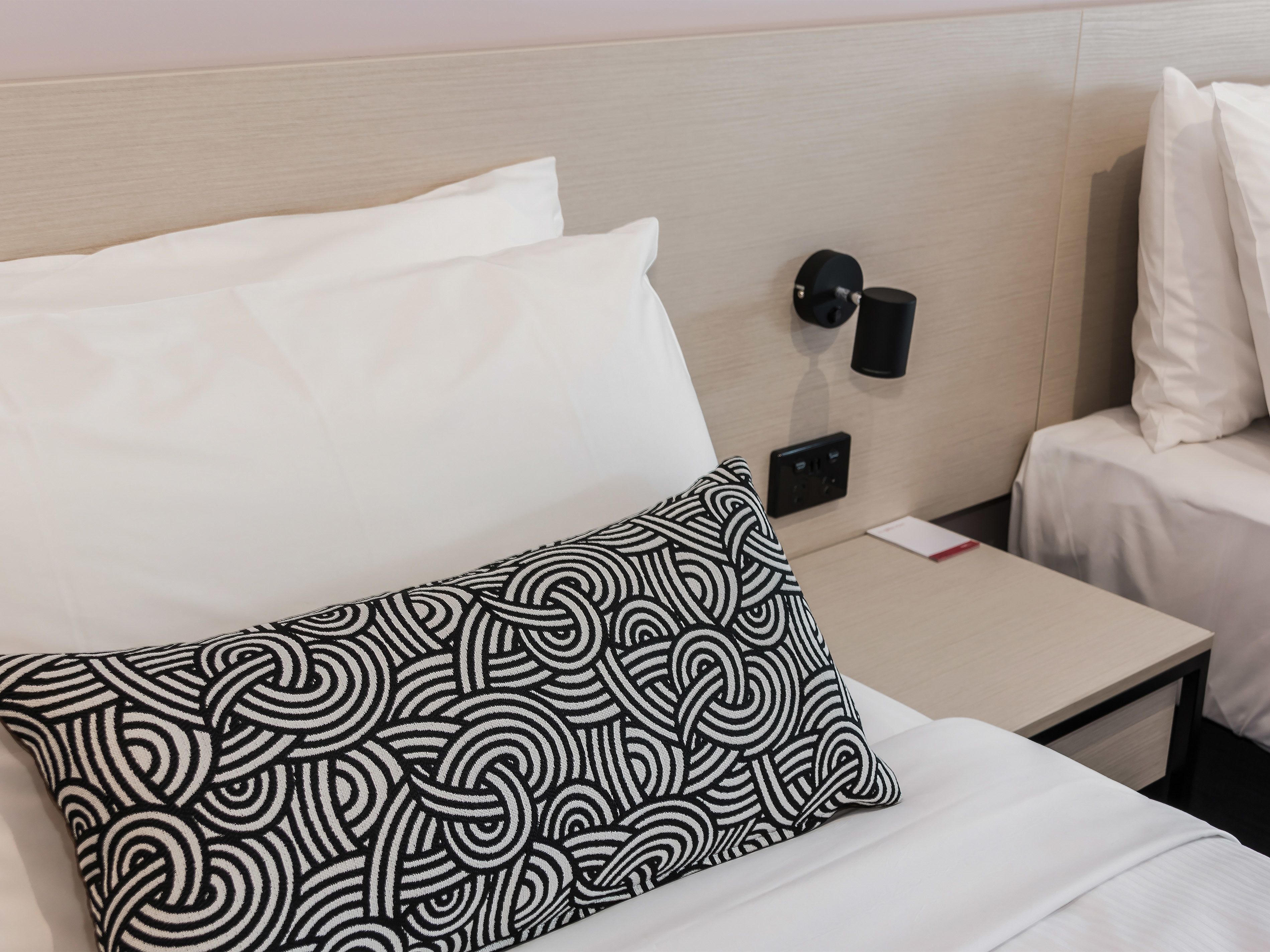 Una cama bien hecha con ropa de cama blanca y una almohada estampada en blanco y negro.