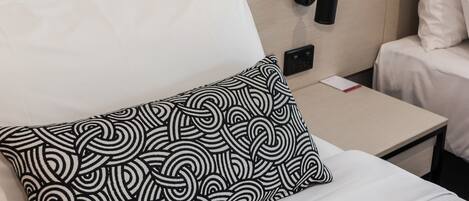 Una cama bien hecha con ropa de cama blanca y una almohada estampada en blanco y negro.
