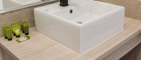 A bathroom with a white sink, black faucet, and a mirror above it. There are green toiletries on the counter.