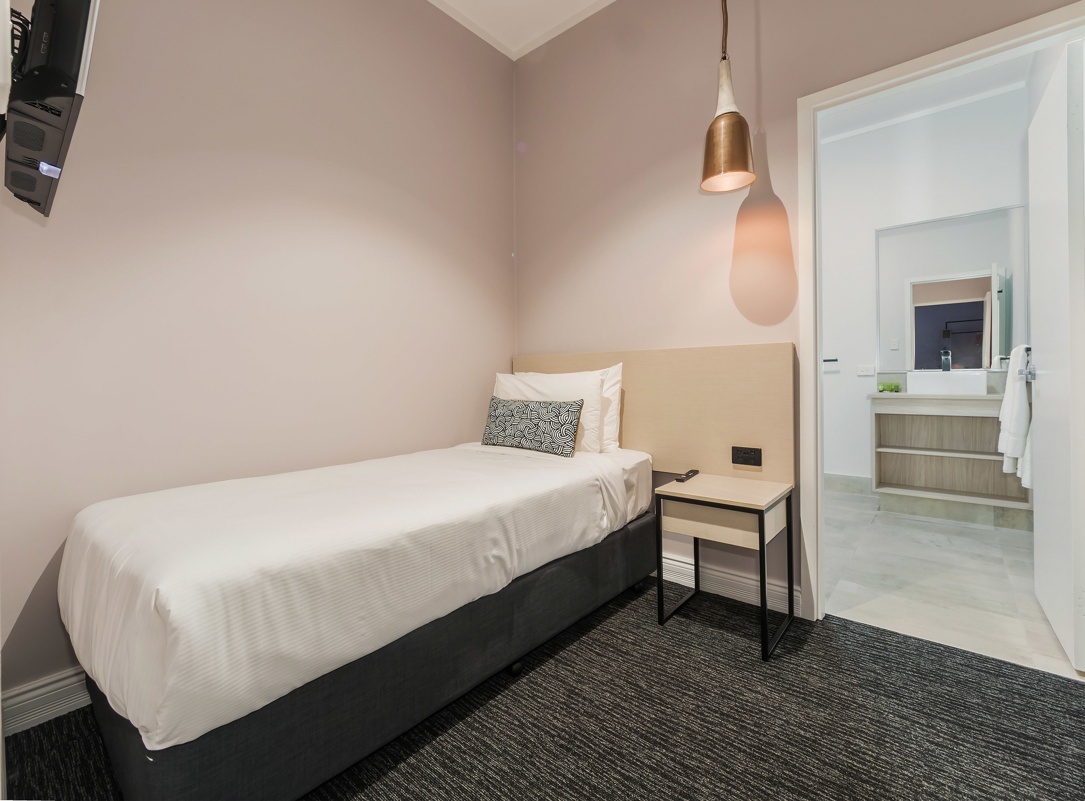 Habitación de hotel ordenada con una cama individual, mesita de noche y una lámpara colgante.