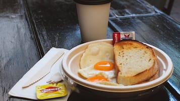 Un plato con tostadas, un huevo frito y una porción de Vegemite, acompañado de una taza de café y una servilleta sobre una mesa de madera.