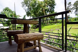 A wooden bench and table on a balcony with a view of a green landscape and purple flowers. - Phu Pha View Doi (Samoeng)