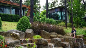 A garden with a stone waterfall, lush greenery, and a modern building in the background. - Phu Pha View Doi (Samoeng)