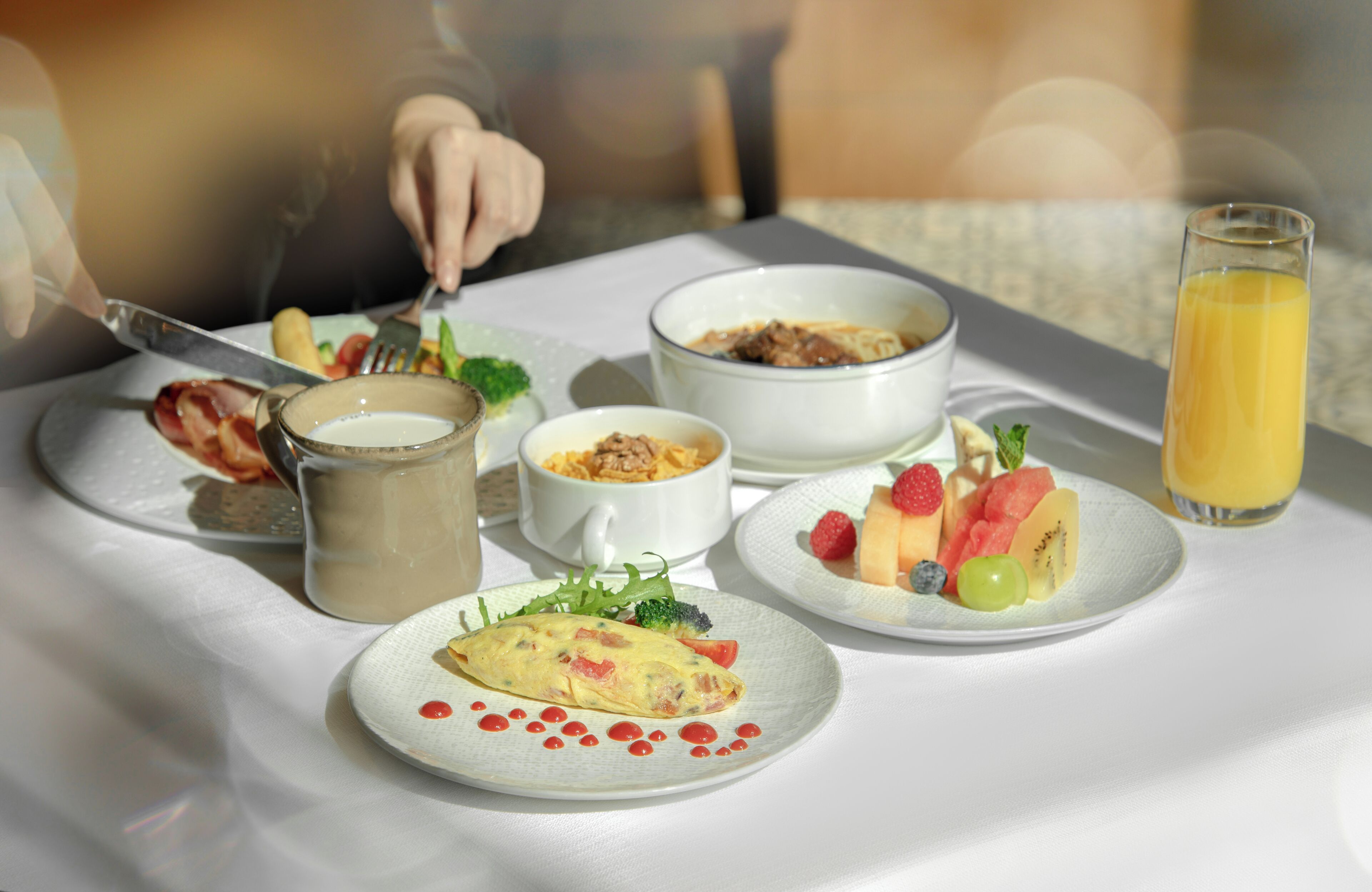 Ein Frühstückstisch mit verschiedenen Speisen, darunter ein Omelett, Obst, Müsli und ein Glas Orangensaft.