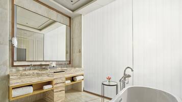 A modern bathroom with a marble vanity, a large mirror, a freestanding bathtub, and a small table with a vase.